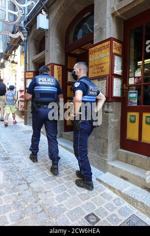 Mont St Michel, Francia: Agosto 2020: Due poliziotti che indossano maschere e pattugliano le strade all'interno delle mura della città di Mont St Michel, Francia Foto Stock