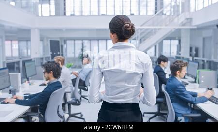 Back View Shot di una bella donna Manager è camminare tra due file dei suoi colleghi di affari e supervisionare il loro lavoro. Diversificati e motivati Foto Stock