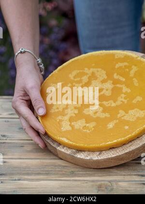 Donna che tiene un pezzo arrotondato giallo di cera d'api fusa su un tavolo di legno. Spazio di copia Foto Stock