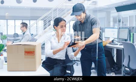 Happy Delivery Man entra in Corporate Office, Hands Package a una bella Businesswoman, firma la sua firma sul Tablet computer. Grande luminoso Foto Stock