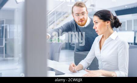 Beautiful Businesswoman usa il computer desktop, consulta il suo Project Manager su documenti con grafici e statistiche. In background Big Foto Stock