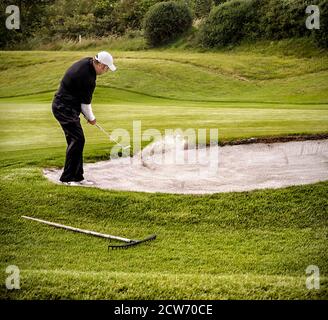 Golfer che tenta di colpire la palla fuori dal bunker sul fairway. Foto Stock