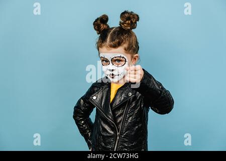 Headshot di bambina con espressione seria, indica alla macchina fotografica con il dito anteriore, indossa trucco creativo, isolato su sfondo blu, vestito io Foto Stock