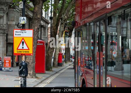 LONDRA - 12 SETTEMBRE 2020: Cartello di avvertimento alberi bassi con il lato di un autobus Red London Double Decker che passa e la vecchia scatola del telefono e posta nel Foto Stock