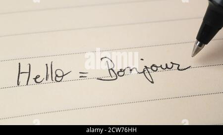 Principiante studente di lingua francese che scrive Ciao parola Bonjour per i compiti su uno scatto macro del notebook Foto Stock
