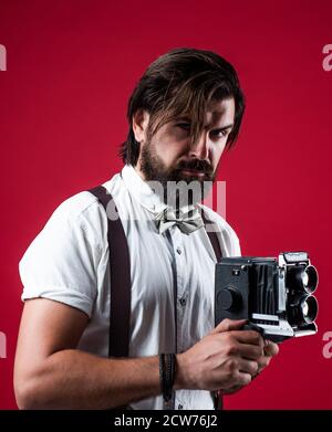 giornalista con fotocamera vintage. reporter formale. hipster vecchio stile con bearded. uomo retrò in sospetti e cravatta di prua. fotografo elegante e sicuro tenere fotocamera classica. Foto Stock