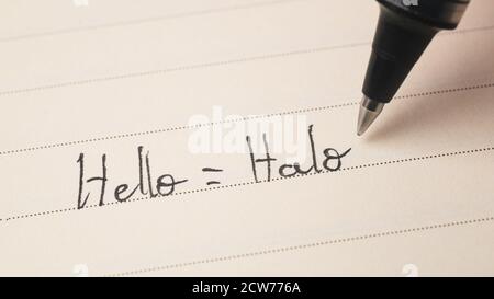 Principiante studente indonesiano di lingua che scrive Ciao parola Halo per i compiti su uno scatto macro del notebook Foto Stock