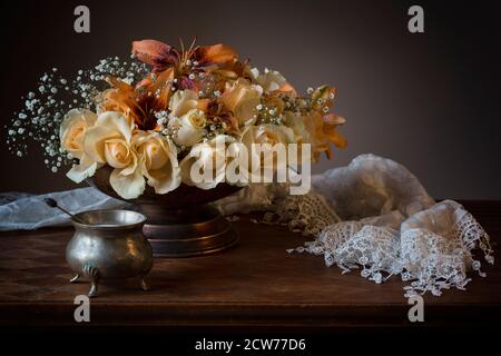 Profumo di natura morta con rose bianche e arancioni cremose e. gigli in una ciotola di peltro con una sciarpa di lacy Foto Stock