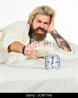 Odiate il risveglio della mattina presto. Pianificazione. Arrivare a letto in tempo. Alzati subito. Sveglia uomo stressata. Ragazzo assonnato e sveglia a letto. Uomo bearded con sveglia. Hipster vuole dormire. Foto Stock