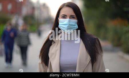 Ritratto di una donna di razza mista nelle strade della città durante il giorno, indossando una maschera viso contro il coronavirus quarantena seconda onda COVID-19 Foto Stock