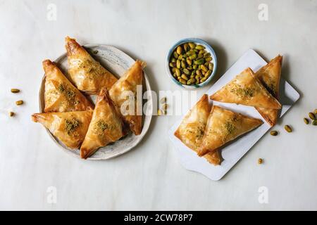 Tradizionale dolce turco fatto in casa baklava con pistacchio servito su tagliere di legno bianco con ciotola di noci su sfondo di marmo bianco. Piatto Foto Stock