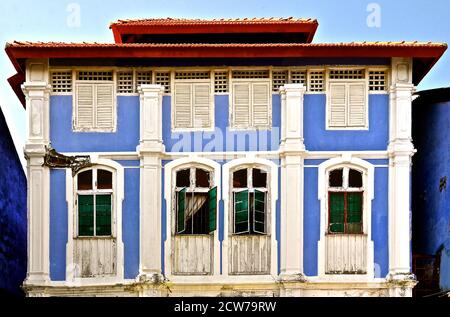 Vecchio edificio in stile peranakan con facciata blu, intonaco bianco e rustiche persiane in legno. Foto Stock