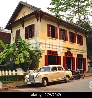 Auto d'epoca color crema parcheggiata all'esterno di un edificio coloniale con persiane in legno rosso. Foto Stock