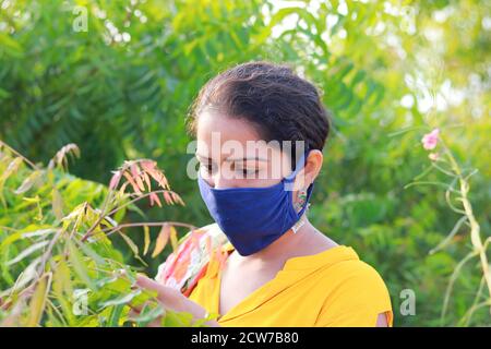 Giovane donna indiana che indossa casa fatta blu maschera prevenzione durante il tempo di corona la raccolta del neem lascia le informazioni Foto Stock