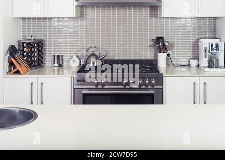 Moderna cucina bianca interna con la stufa e utensili con isola tavolo Foto Stock