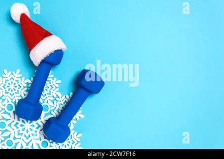 Piatto natalizio con manubri in cappello rosso di Babbo Natale su sfondo blu. Natale e Capodanno concetto di vacanza per fitness, allenamento e sano Foto Stock