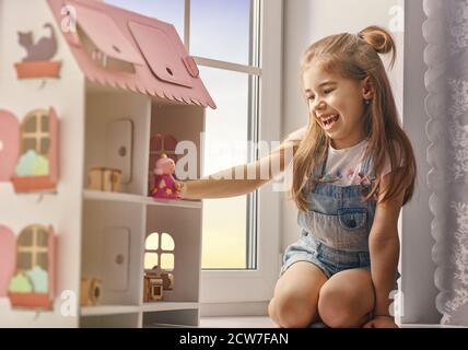 La ragazza felice gioca con la casa della bambola e l'orso del teddy a casa. Divertente, il bambino adorabile si diverte nella camera dei bambini. Foto Stock