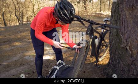 Giovane atleta caucasica ciclista turistica utilizza un attrezzo manuale, una pompa di bicicletta per gonfiare l'aria in una mountain bike gommata. Guasto e rapido Foto Stock
