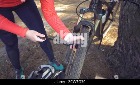 Giovane atleta caucasica ciclista turistica utilizza un attrezzo manuale, una pompa di bicicletta per gonfiare l'aria in una mountain bike gommata. Guasto e rapido Foto Stock