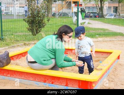 POZNAN, POLONIA - 14 maggio 2016: Donna e bambino non identificati che giocano in una scatola di sabbia su un terreno di gioco in una giornata di sole Foto Stock