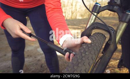 Giovane atleta caucasica ciclista turistica utilizza un attrezzo manuale, una pompa di bicicletta per gonfiare l'aria in una mountain bike gommata. Guasto e rapido Foto Stock