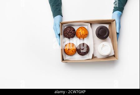 Caffè e dolci di fast food. Cameriere in guanti di gomma dà ordine, muffin al cioccolato e torte in scatola di cartone con tazze di carta da asporto Foto Stock