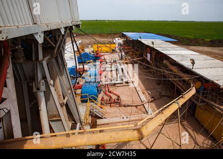 Panorama di deposito di olio e attrezzature. Di carro di perforazione di olio. Tubi e macchine. Campo verde e cielo blu sullo sfondo. Carro di perforazione ad olio (sinistra). Foto Stock