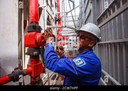 Operaio asiatico adulto in casco da lavoro bianco e valvola di regolazione dell'usura da lavoro blu sul carro di perforazione a olio. Deposito di olio di Zhaik-Munai, Kazakistan Foto Stock