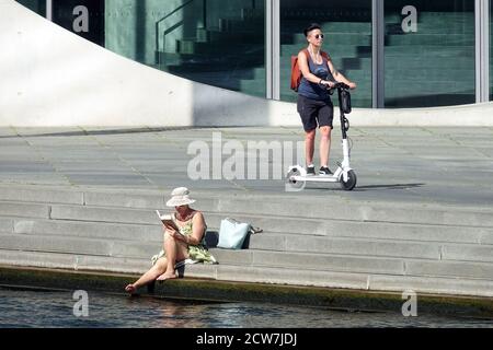 Turisti di Berlino una donna su uno scooter elettrico e un'altra donna sulla riva del fiume Sprea legge un libro, Germania, donna turistica che legge un libro fuori Foto Stock