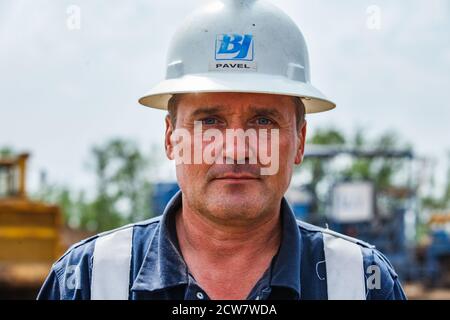 Deposito di olio. Ritratto di un serio operatore petrolifero in posa. Logo aziendale di Baker Hughes su hardhat. E nome Pavel. Foto Stock