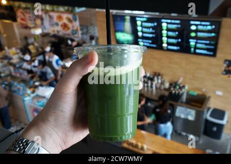 Chiudere la mano tenendo una tazza di plastica da togliere di Tè freddo Matcha verde Foto Stock