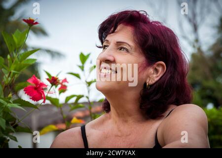 Ritratto di una bella donna latina di mezza età all'aperto dentro il giardino con i suoi capelli appena tinti in un piatto colore Foto Stock