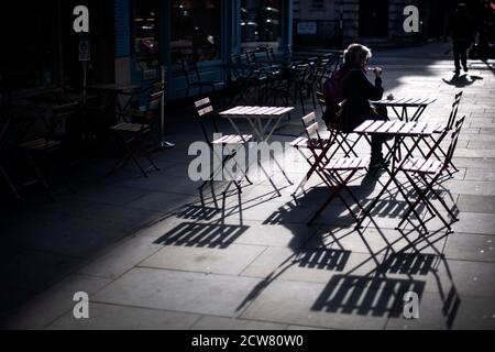 Una donna cena da sola su posti a sedere all'aperto fuori di un ristorante a Covent Garden, Londra, dopo una serie di nuove restrizioni per combattere l'aumento dei casi di coronavirus è entrato in vigore in Inghilterra. Foto Stock