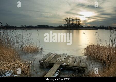 Una piattaforma di legno nelle canne sulla riva di un lago ghiacciato Foto Stock