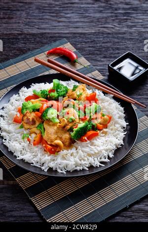 Pollo alla cashew tailandese con verdure saltate in padella: Broccoli, pepe dolce, peperoncino rosso caldo e salsa di soia serviti su un piatto nero con riso e chopsticks o Foto Stock