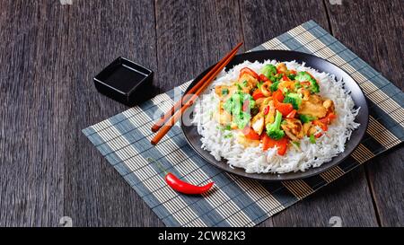 Pollo alla cashew tailandese con verdure saltate in padella: Broccoli, pepe dolce, peperoncino rosso caldo e salsa di soia serviti su un piatto nero con riso e chopsticks o Foto Stock