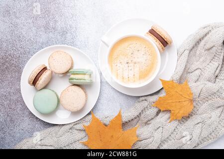 Accogliente composizione autunnale con maglione, caffè, vari macaron e foglie di acero giallo su fondo di pietra. Disposizione piatta, vista dall'alto - immagine Foto Stock