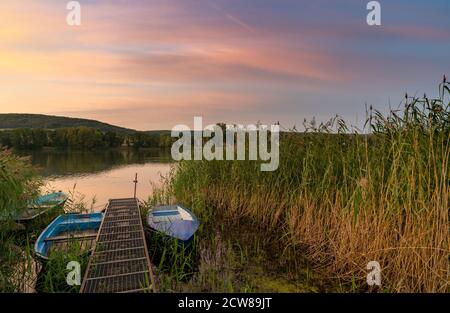 Un colorato tramonto sul paesaggio del lago con piccole barche a remi il primo piano Foto Stock