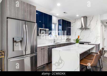 Una cucina moderna con armadietti blu e in legno a due tonalità con una cascata di marmo bianco cima dell'isola e backsplash. Foto Stock