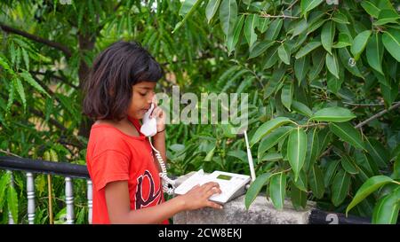 Ragazza indiana dei bambini che usa il telefono. Concetto di casa da sola Foto Stock