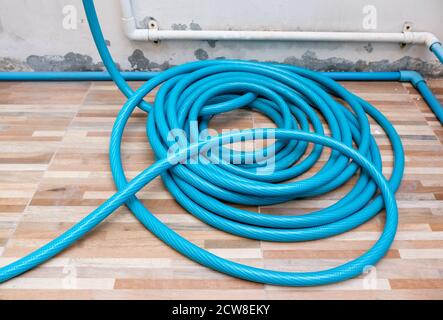 Rotolo di tubo di irrigazione in gomma è posato sul pavimento in piastrelle vicino alla terrazza della casa urbana. Foto Stock