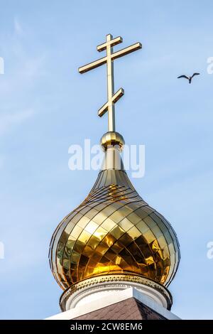 la cupola della chiesa con una croce contro il cielo blu con un uccello volante Foto Stock