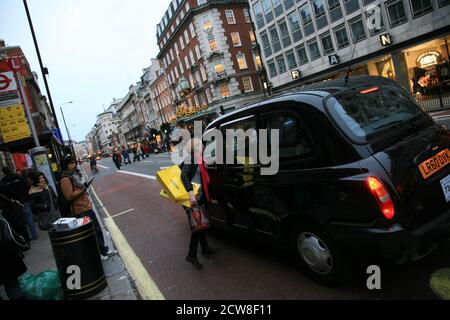 Londra, Regno Unito - 13 novembre 2010: Taxi nella strada di Londra. Passeggero donna con borse per la spesa che chiede all'autista prima di salire a bordo. Le cabine nere sono il Foto Stock