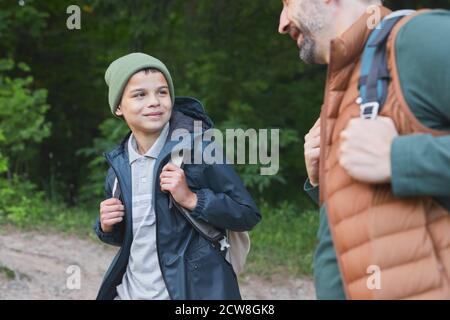 Vita in su ritratto di padre felice e figlio che camminano insieme e guardarsi l'un l'altro mentre camminando nella foresta con i pali di trekking, spazio di copia Foto Stock