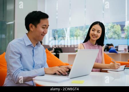 Uomo d'affari e donna asiatici sorridenti e che lavorano insieme, scrivendo in taccuino, collaborazione, collaborazione, lavoro di squadra Foto Stock