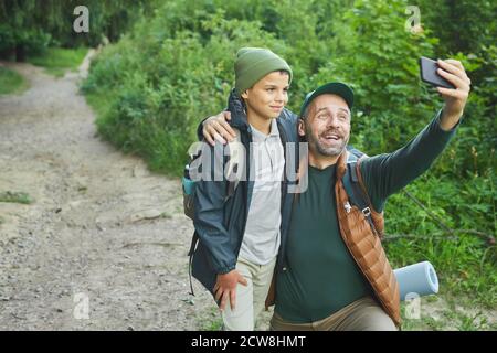 Ritratto di padre e figlio camminando insieme e scattando foto selfie via smartphone, copia spazio Foto Stock