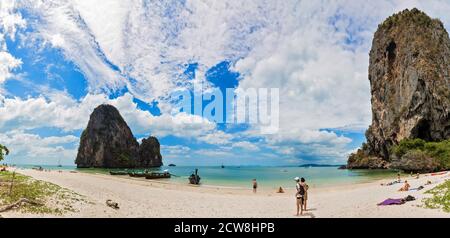 Panorama completo di PhraNang Cave Beach e Thaiwand Wall nel mare delle andamane. Spiaggia di sabbia con turisti a piedi e nuoto, barche a coda lunga, montagna e cielo blu con le nuvole Foto Stock