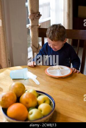 il ragazzo di 2 anni grida dopo aver versato il latte sul tavolo da cucina. ©Bob Daemmrich Foto Stock