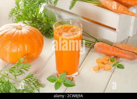 Succo di carota e zucca appena spremuto in un bicchiere sopra uno sfondo di legno con carote fresche Foto Stock