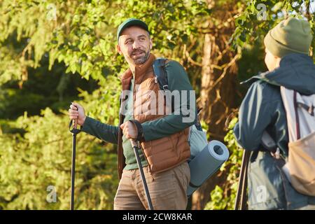 Ritratto di felice padre e figlio camminando insieme e parlando mentre camminando nella foresta con i pali, spazio di copia Foto Stock